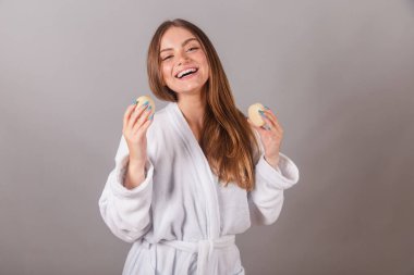 Bornoz giymiş güzel Brezilyalı kadın, cilt bakımı için iki sabun tutuyor..