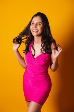 Brezilyalı kadın, pembe elbiseli, sarı fotografik arka planda, dikey fotoğrafta poz veriyor..