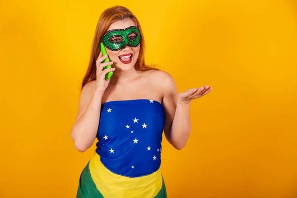 ブラジルの国旗で作られたカーニバルの服を着た美しい赤い髪のブラジル人女性が携帯電話で声をかけて — ストック写真