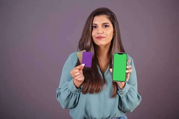 Horizontal photo. Beautiful Brazilian woman, with casual clothes, Jeans and green shirt. smartphone with green screen and cards.
