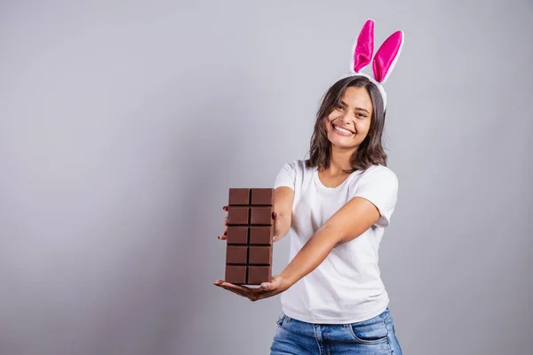 巴西女人 带着复活节兔子的耳朵 快乐地微笑着 手里拿着复活节巧克力棒 — 图库照片