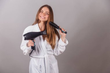 Harika saçları olan Brezilyalı sarışın kadın. Bornoz giymişti. Saç kurutma makinesi ve saç fırçası kullanarak..