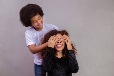 Afrikalı Amerikalı bir çocuk annesini kapalı tutuyordu. Gri arkaplan. Anneler Günü. Brezilyalı aile.