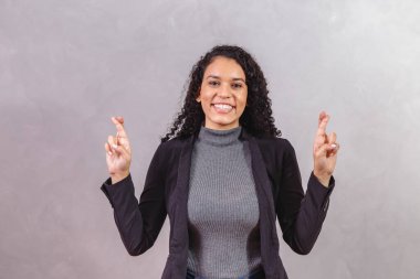 Genç kadın parmaklarını çapraz yapıp, gri arka plana bakıyor.