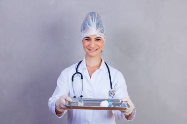 Hemşire, gri arka planda ilaçlı tepsiyi tutuyor. Gri arka plandaki doktorlar. Aşı ve ilaç. Sağlık ve bakım kavramı