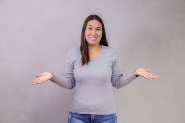 Gri arka planda kafası karışmış genç bir kadın ve mesaj için yeri var. Gri arka planda soyutlandığını bilmediğini söyleyen ellerini uzatan bir kadın. Hiçbir fikrim yok.