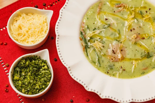 おいしいブロッコリーの緑のスープ 緑のブロッコリーのスープ ベジタリアン すりおろしたパルメザンチーズとパセリ 木製の背景と赤い生地 ブラジルの冬の食べ物 — ストック写真