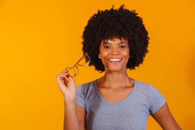 Kameraya gülümseyen gözlüklü afro kadın.