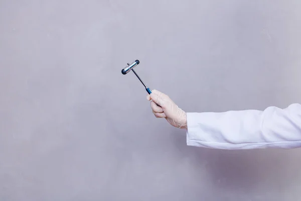 The doctor is holding a neurological hammer on a grey background. The neurologist checks the patient's reflexes with a hammer. Diagnostics, healthcare, and medical care