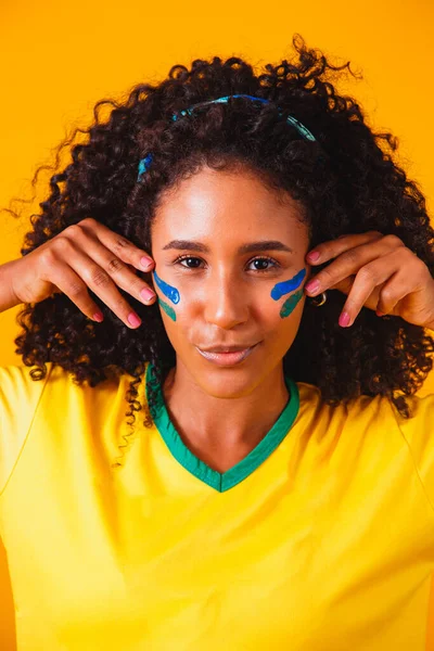 Brazilian fan. using paint as makeup, Brazilian fan celebrating football or soccer game on yellow background. Colors of Brazil.