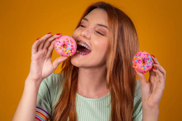 红头发的黄种女孩吃着美味的彩色甜甜圈 — 图库照片