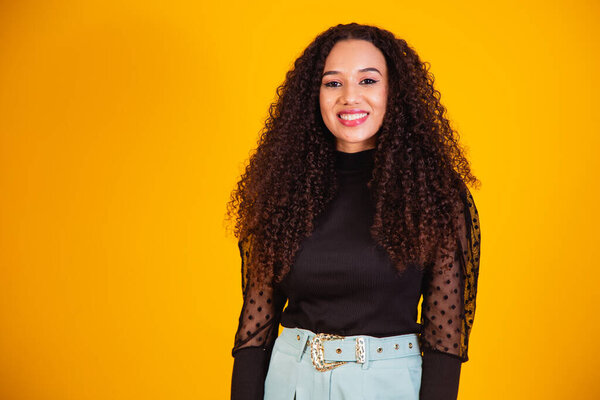 Beauty portrait of a Brazilian woman with afro hairstyle and glamour makeup. Latin woman. Mixed race. Curly hair. Hair style. Yellow background