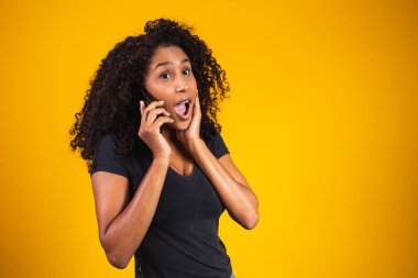 Sarı arka planda cep telefonuyla konuşan mutlu Afro-Amerikan genç kadın portresi.
