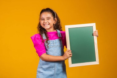 Esmer çocuk sarı arka planda kara tahta tutuyor..