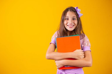 Okula giderken elinde kitaplarla gülümseyen güzel bir kız. yakın plan, izole edilmiş sarı arka plan, çocukluk. Çocuk kucaklama defterleri. Yaşam tarzı, ilgi, hobi, boş zaman, boş zaman
