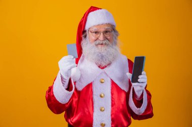 Elinde kredi kartı ve elinde boş ekranla elinde akıllı telefon tutan yakışıklı bir Noel Baba portresi..