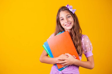 Okula giderken elinde kitaplarla gülümseyen güzel bir kız. yakın plan, izole edilmiş sarı arka plan, çocukluk. Çocuk kucaklama defterleri. Yaşam tarzı, ilgi, hobi, boş zaman, boş zaman