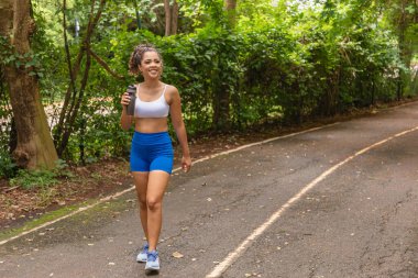 Parkta yürüyen ve su içen Afro genç bir kadın..