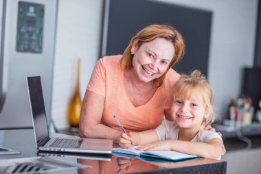 Gülümseyen olgun bir anne, kızına ev işleri hazırlamada yardımcı olur. Çevrimiçi eğitim kavramı.