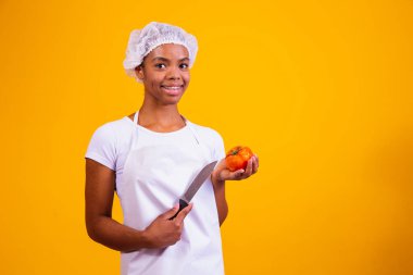 Elinde bıçak ve domates tutan önlüklü bir kadın..