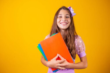 Okula giderken elinde kitaplarla gülümseyen güzel bir kız. yakın plan, izole edilmiş sarı arka plan, çocukluk. Çocuk kucaklama defterleri. Yaşam tarzı, ilgi, hobi, boş zaman, boş zaman