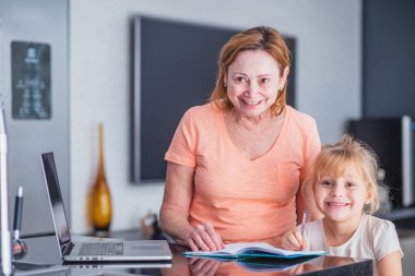 Gülümseyen olgun bir anne, kızına ev işleri hazırlamada yardımcı olur. Çevrimiçi eğitim kavramı.