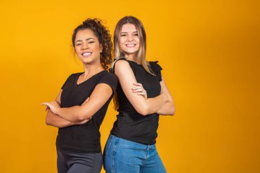 Sarı arka planda sarışın ve afro kız arkadaşlar. Beyaz sarışın bir kadın ve afro esmer, çeşitlilik kavramı.