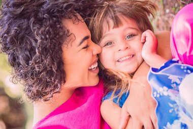 Sevgi dolu genç bir anne ve kızı birbirlerine sevgi gösteriyorlar. Anne ve kızı parkta. Anneler Günün kutlu olsun.