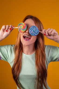 Gözlerini bağlayan renkli lolipopları olan kızıl saçlı genç bir kadın. moda konsepti