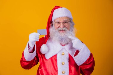 Noel Baba 'nın sarı arka planda kredi kartı tutarken çekilmiş bir fotoğrafı. Kredi kartı ya da banka kartı ile kolay ödeme kavramı. banka ödemesi