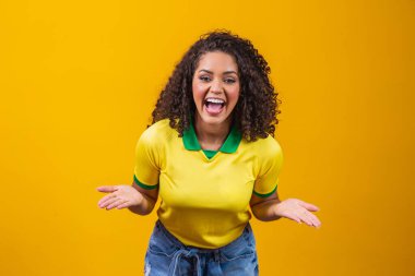 Brezilya taraftarı. Brezilyalı kıvırcık saçlı kadın fanatik futbolu, sarı arka planda futbol maçını kutluyor. Brezilya renkleri.