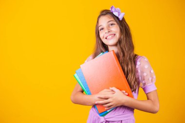 Okula giderken elinde kitaplarla gülümseyen güzel bir kız. yakın plan, izole edilmiş sarı arka plan, çocukluk. Çocuk kucaklama defterleri. Yaşam tarzı, ilgi, hobi, boş zaman, boş zaman