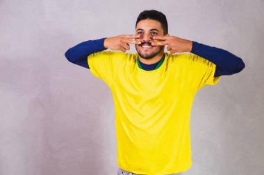 Brezilyalı bir hayran. Brezilya taraftarı, boyanın makyaj malzemesi olarak gri arka planda futbol ya da futbol maçını kutluyor. Brezilya 'nın Renkleri.