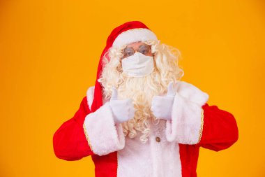 Sarı arka planda gerçek Noel Baba, Covid19 'a karşı koruyucu maske takıyor. Sosyal mesafeli bir Noel. Covid 19