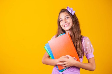 Okula giderken elinde kitaplarla gülümseyen güzel bir kız. yakın plan, izole edilmiş sarı arka plan, çocukluk. Çocuk kucaklama defterleri. Yaşam tarzı, ilgi, hobi, boş zaman, boş zaman
