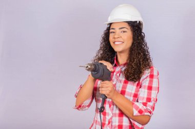 Beyaz arka planda elektrikli matkap tutan afro bir kadın..