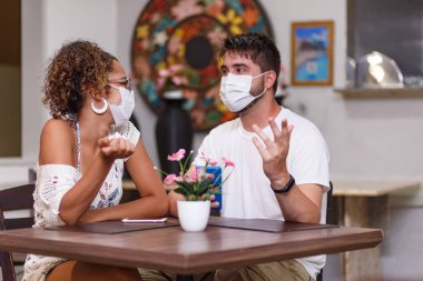 Bir kaç arkadaş açık hava restoranında oturmuş güvenlik maskesi takarak Coronavirus salgınına karşı güvenlikten bahsediyorlar. Yeni normal yaşam konsepti