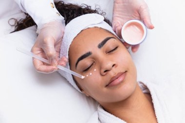 Yüzünde krema ve yanında kavanoz olan güzel bir kadının yakın çekimi. Yüz kremi süren bir kadın. spa konsepti