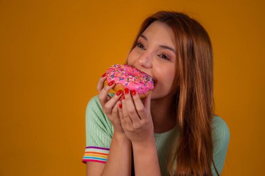 Sarı arka planda pembe çörek yiyen kız..