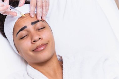 Estetik ameliyat. Genç Afrikalı kadın güzellik kliniğinde kaş bölgesinde botoks yaptırıyor. Yakın plan, fotokopi odası. Genç Afrikalı kadın alnına botoks yaptırıyor..