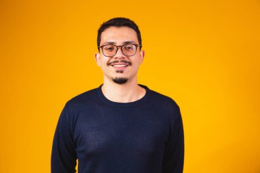 Gözlüklü bir adamın, sarı arka planda izole edilmiş, gülümseyerek kameraya baktığı bir fotoğraf.