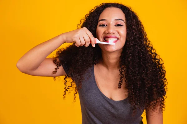 黄色の背景に歯を磨く若いアフロの女の子 アフロの女は歯を磨く 口腔衛生の概念 — ストック写真