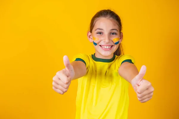 美しいです小さなブラジルのファン女の子とともに親指アップギブアップ上の黄色の背景に絵の顔 — ストック写真