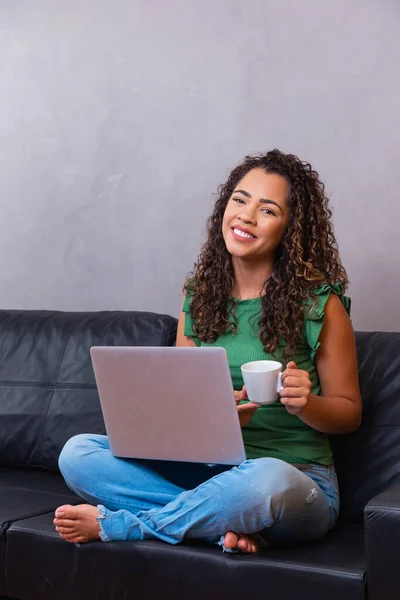 用笔记本电脑微笑的非洲女青年 坐在家里的沙发上 漂亮的女孩购物或在社交网络上聊天 开心的看电影 做电脑项目的自由职业者 — 图库照片