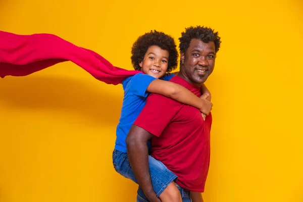 非洲父亲和儿子在白天扮演超级英雄 黄色背景有趣的人 友好家庭的概念 — 图库照片