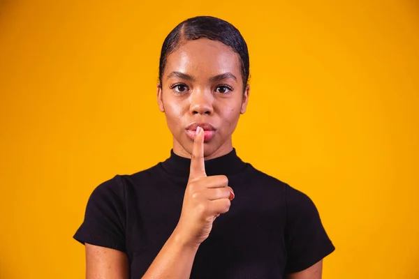 Secret, gossip concept. Young woman whispering a secret behind her hand. Business woman isolated on trendy yellow studio background. Young emotional afro woman. Human emotions, facial expression
