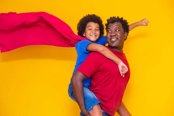 非洲父亲和儿子在白天扮演超级英雄 黄色背景有趣的人 友好家庭的概念 — 图库照片