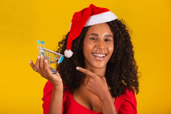 サンタの帽子の女性はクリスマスショッピングをしています 彼女はミニカートを見せている — ストック写真