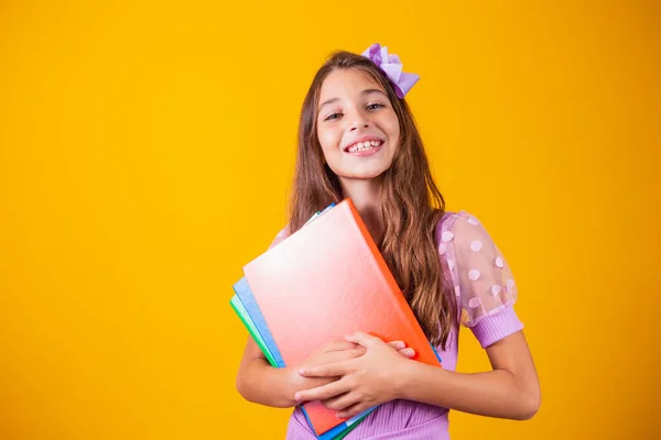 stock image Beautiful smiling girl holding books going to school. close up portrait, isolated yellow background, childhood. child hugging notebooks. lifestyle, interest, hobby, free time, free time