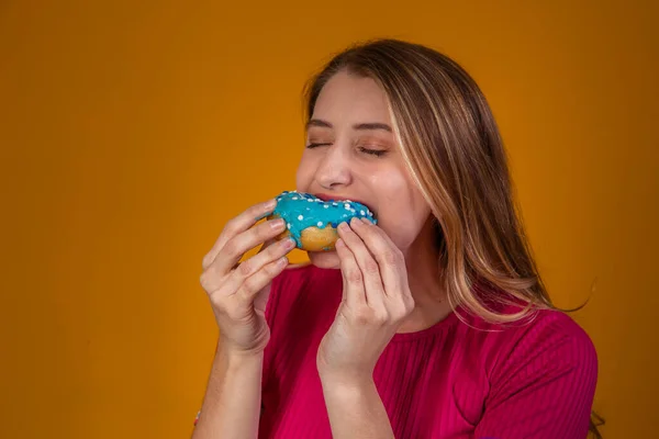 一个年轻的金发女孩吃着美味的彩色甜甜圈的画像 — 图库照片